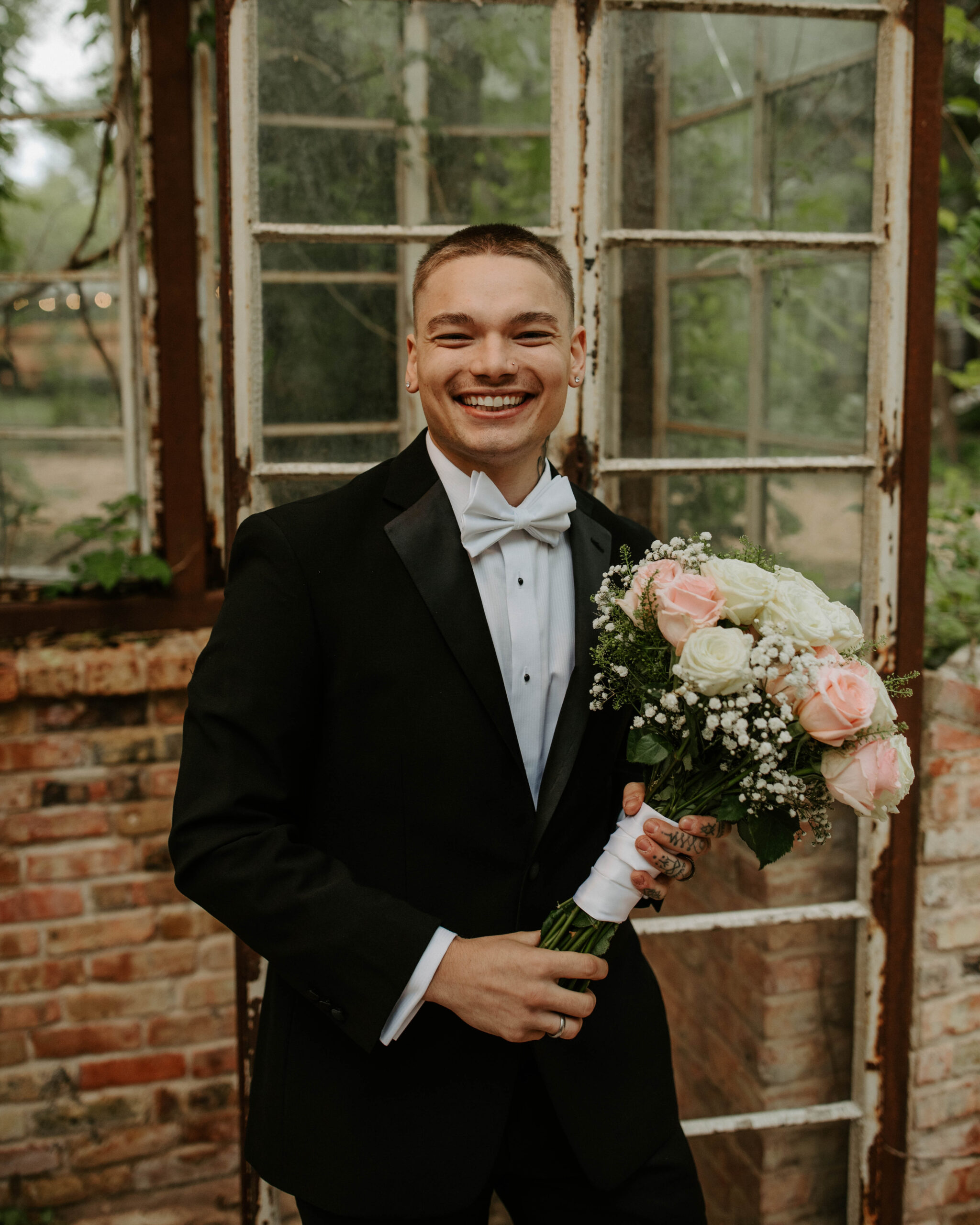 Groom in black suit holding bridal bouquet at Sekrit Theater.