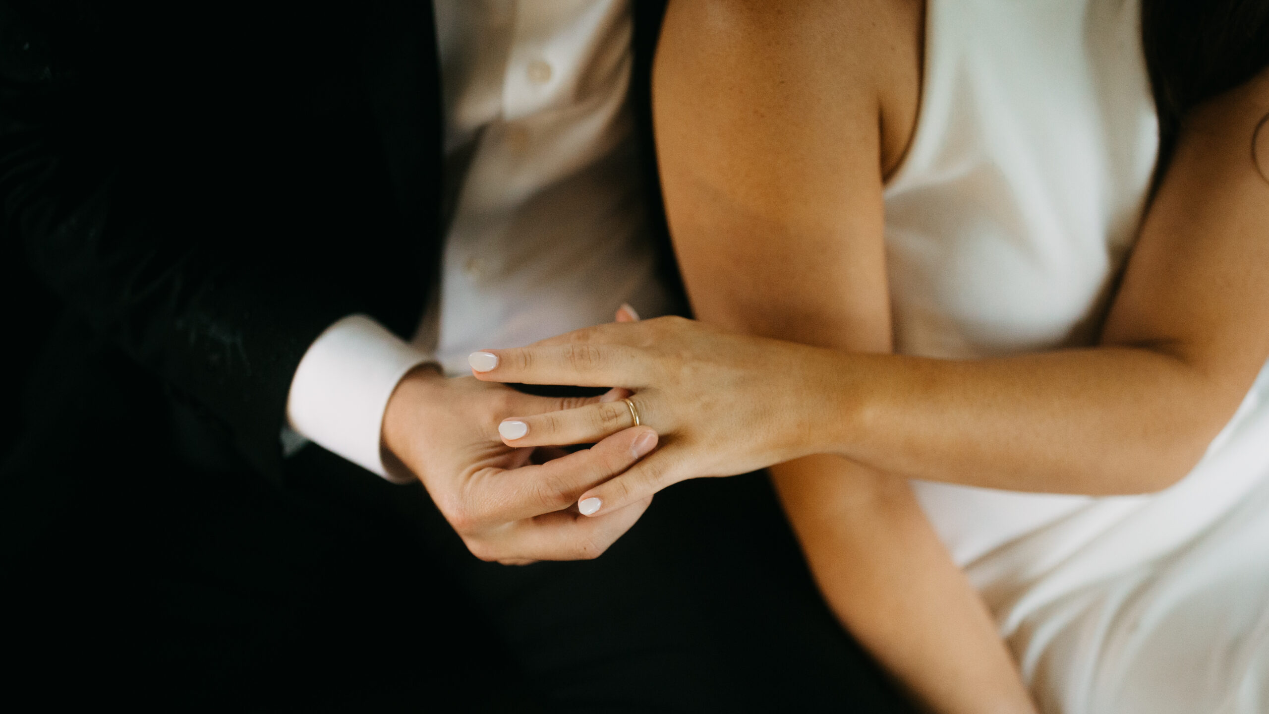 A groom putting gold wedding ring on bride's finger.