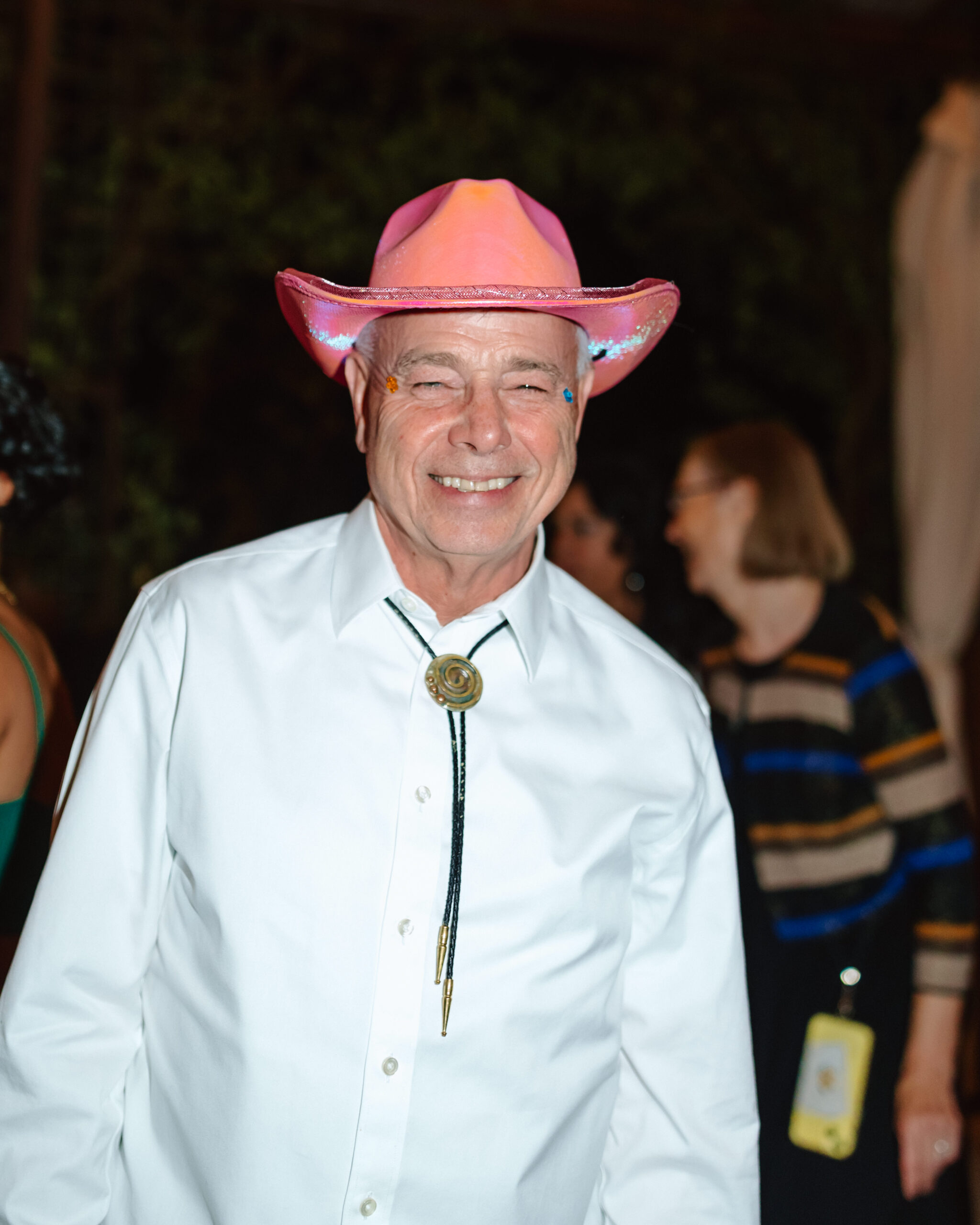 Man smiling at anwedding reception while wearing a pink cowboy hat.